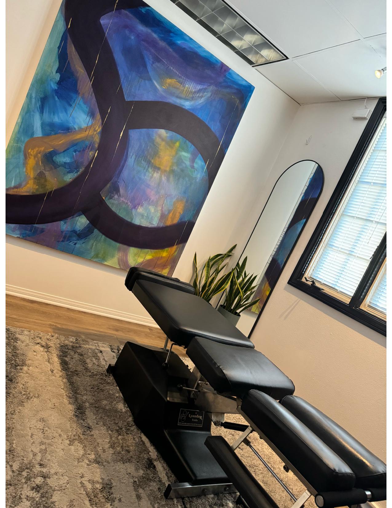 Treatment room with chiropractic table and original artwork